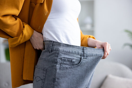 Woman standing, pulling out oversized jeans at the waist, demonstrating significant body transformation and weight loss through healthy diet and fitness
