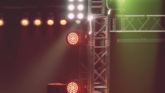 Bright lights shine on a music stage during an event in the evening. The setup includes metal structures and various lights showing a vivid display.