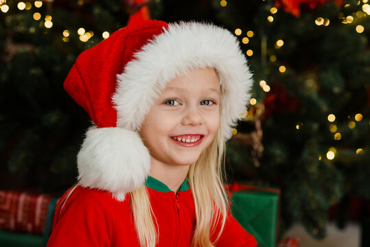 Merry Christmas and Happy Holidays. Child girl in Santa Claus hat with gifts under Christmas tree
