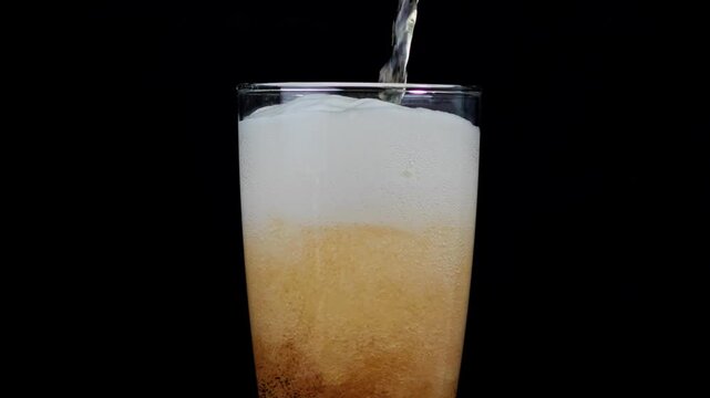 Beer pouring from bottle into glass with thick foam overflow.