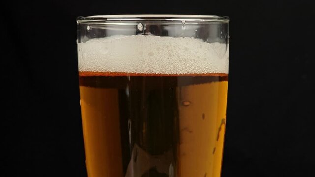 A glass filled with amber beer on black background.