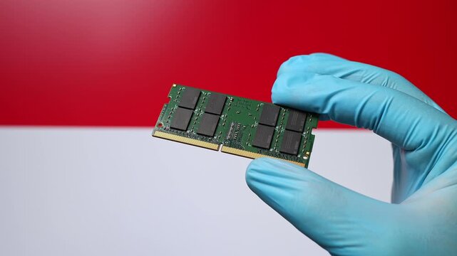 Close up view of hand in blue glove holding RAM memory microchip module. Indonesian flag in blurred background. Concept of semiconductor shortage and artificial intelligence development in Indonesia.