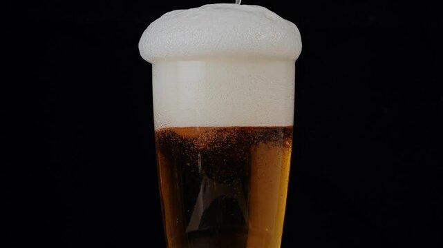 Beer pouring from bottle into glass with thick foam overflow.