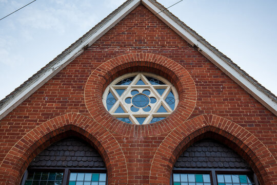 Close up of a hexagram star of david window set into red brick arches on a gable
