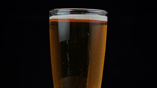 A glass filled with amber beer on black background.