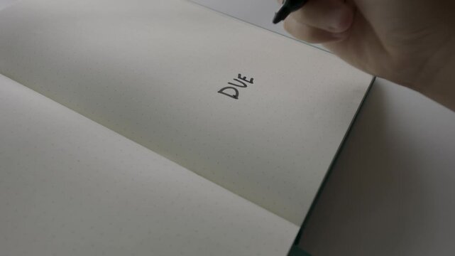 Person writing due asap with black marker on dotted notebook page.