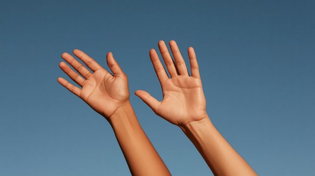 Two raised hands reaching upward against a clear blue sky  