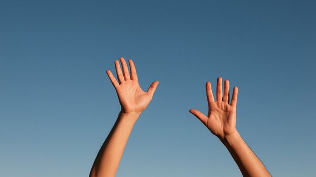 Two raised hands reaching upward against a clear blue sky  