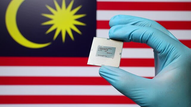 Close up view of hand in blue glove holding CPU microchip. Malaysian flag in blurred background. Concept of semiconductor shortage and artificial intelligence development in Malaysia.