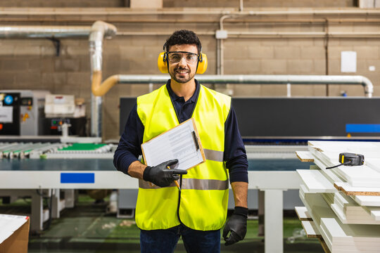 Factory worker holding clipboard smiling in lumberyard