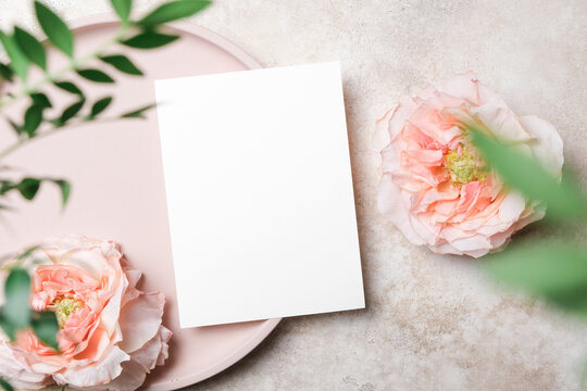 Blank wedding invitation or greeting card mockup on beige background with fresh roses and green leaves. Elegant floral flat lay for menu or invitation card design
