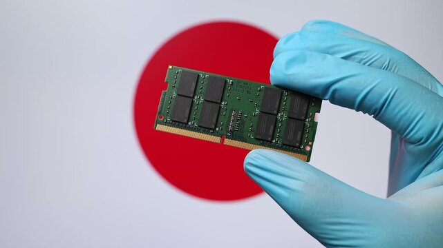 Close up view of hand in blue glove holding RAM memory microchip module. Japanese flag in blurred background. Concept of semiconductor shortage and artificial intelligence development in Japan.