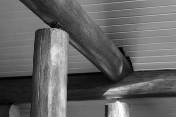 Naklejka premium Monochrome close-up of rustic wooden beams and round log columns supporting a paneled ceiling, highlighting timber grain, joinery and texture in an interior architectural study