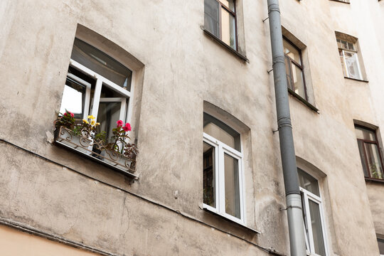 Weathered apartment facade with open windows and colorful flower boxes, showing urban charm and rustic textures of old Saint-Petersburg town