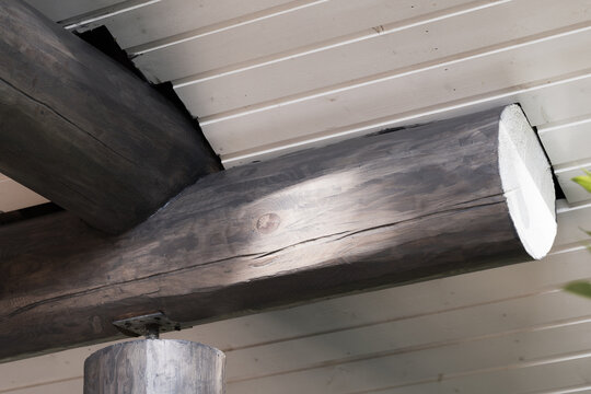 Close-up view of a rustic wooden beam and log ceiling showing timber grain, knots and joint details in porch architecture. Natural texture and structural support convey craftsmanship
