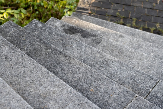 Granite outdoor steps descend toward a paved garden walkway, revealing weathered texture, scattered pine needles and subtle moss. Neutral tones and strong leading lines of minimalist architecture