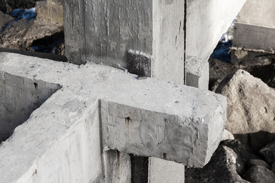 Rough poured concrete foundation blocks at a construction site showing cracked texture, rust stains and surrounding rubble, conveying industrial strength, weathering and structural pier details