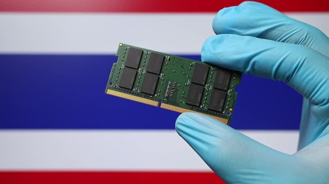 Close up view of hand in blue glove holding RAM memory microchip module. Thai flag in blurred background. Concept of semiconductor shortage and artificial intelligence development in Thailand.