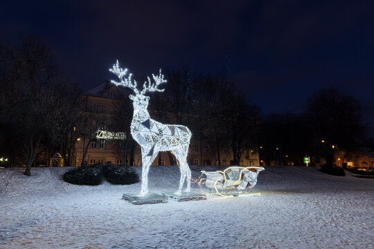 Giant glowing LED reindeer and sleigh installation on snow covered ground at night. Festive Christmas holiday street decoration in winter park, outdoor Christmas light.
