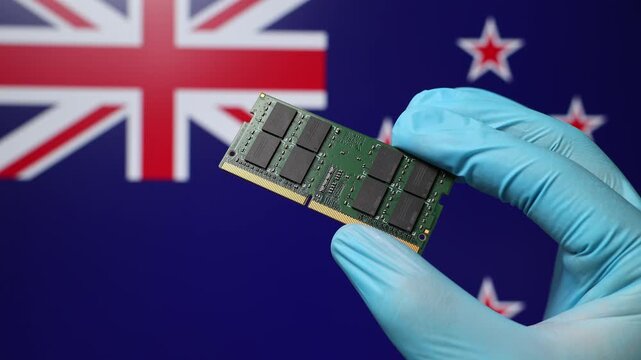 Close up view of hand in blue glove holding RAM memory microchip module. New Zealand flag in blurred background. Concept of semiconductor shortage, artificial intelligence development in New Zealand.