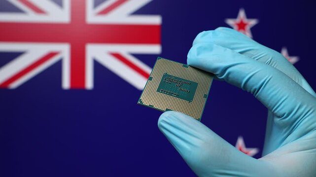 Close up view of hand in blue glove holding CPU microchip. New Zealand flag in blurred background. Concept of semiconductor shortage and artificial intelligence development in New Zealand.