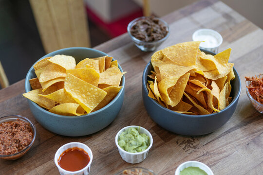 Mexican nachos and crispy corn tortilla chips served with assorted colorful dipping sauces on plates and bowls on a rustic table, perfect for sharing and festive gatherings