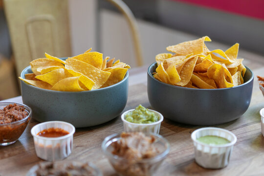 Mexican nachos and crispy corn tortilla chips served with assorted colorful dipping sauces on plates and bowls on a rustic table, perfect for sharing and festive gatherings