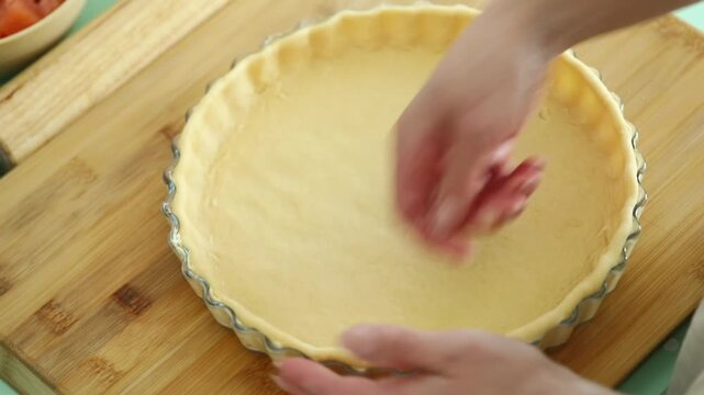 Woman preparing homemade quiche by placing fresh pastry dough into a baking dish in a kitchen.