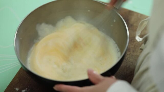 Woman whisking milk and eggs together in a bowl while preparing ingredients for cooking or baking. Homemade food preparation scene 