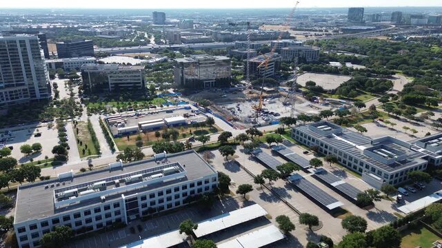 Yellow tower cranes anchor Hall Park development plots near Dallas North Tollway ramps. Active building excavations border solar-covered parking lots along Internet Boulevard, Frisco, Texas