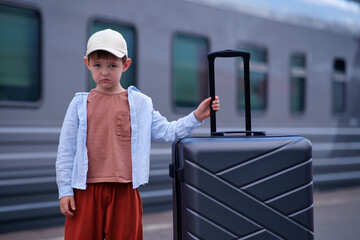 Sad child standing with suitcase on railway platform. Little boy waiting for train travel. Journey, loneliness and vacation concept. Tourism and transportation theme. Back to school trip. © Андрей Журавлев