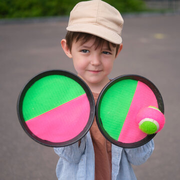 Child holding sticky velcro toss and catch game set with ball. Boy playing outdoor backyard sport activity. Summer recreation, active leisure, fun childhood lifestyle and hobby concept.