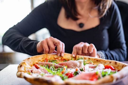 Girl eating prosciutto pizza in a cozy pizzeria with fresh toppings and a friendly atmosphere
