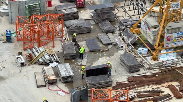 Construction site with workers and heavy machinery, materials scattered around. Workers in high-visibility vests are busy on a large construction site, surrounded by building materials and heavy equip