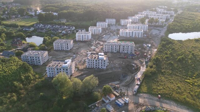 n aerial video showing a large-scale residential development project, with multiple apartment buildings in various stages of construction alongside completed housing units, situated amidst natural pon