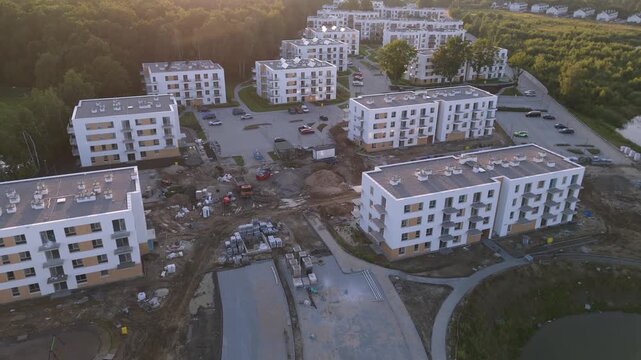 An aerial video showing a large-scale residential development project, with multiple apartment buildings in various stages of construction alongside completed housing units, situated amidst natural po