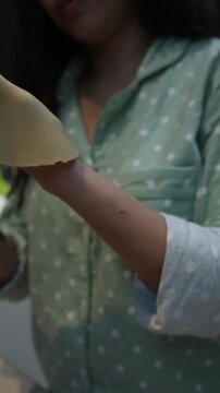 Young woman in green polka-dot shirt kneading and rolling dough to make chapatis in a home kitchen. Close-up of hands working with flatbread dough on a light surface, focused and concentrated expressi