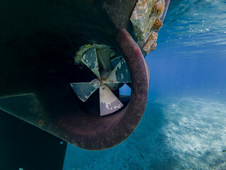 Underwater perspective of a yacht propeller and rudder in clear blue seawater, showing marine equipment, hull inspection, biofouling and boat maintenance with copy space © JairoMZ