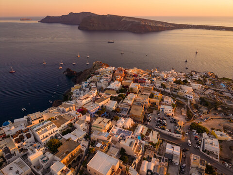 Aerial drone view of white village rooftops and the volcano caldera in background at golden hour, Oia, Santorini, Greece
