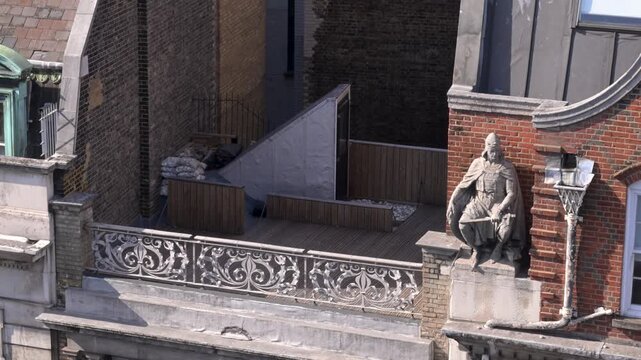 Richard Garbe statue sits on the ornate facade and rooftop terrace of Kingsgate House in High Holborn, London, viewed from an elevated angle on a sunny day.