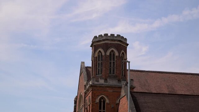 Camera tilts up to the brick tower and roofline of Marlborough Road Methodist Church framed against a soft blue sky.