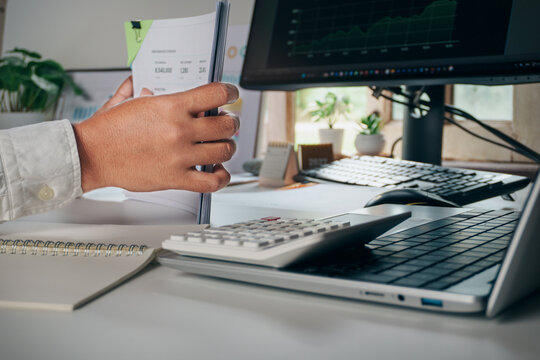 Business professional holding and reviewing business performance report documents on office desk with laptop and calculator, concept of financial data analysis, auditing, and corporate management.