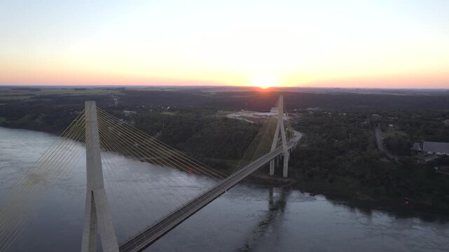 4K drone aerial view of the Integration Bridge at sunset, connecting Paraguay and Brazil across the Paran&aacute; River near the Triple Frontier. Warm evening light illuminates the bridge and surrounding lan