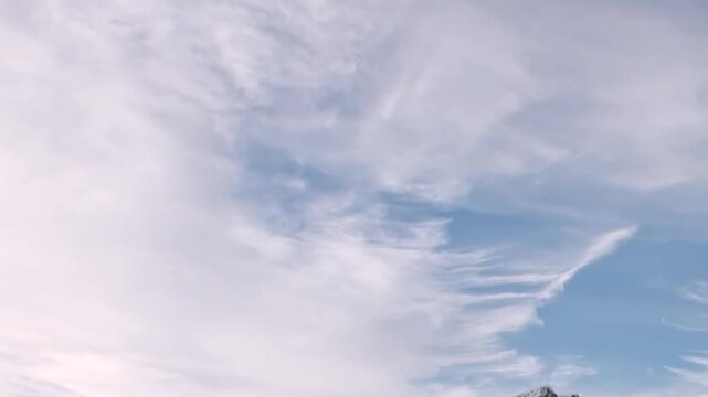 Vast Arctic Ocean expanse unfolds, mirroring an ethereal blue sky filled with wispy white clouds. A distant landmass barely peeks above the horizon, hinting at extreme travel.