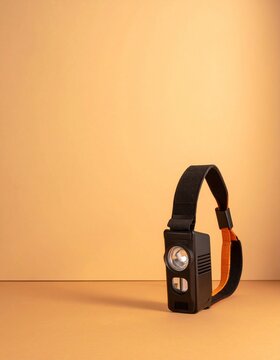 Plain black head torch with an orange strap resting against a warm cream wall