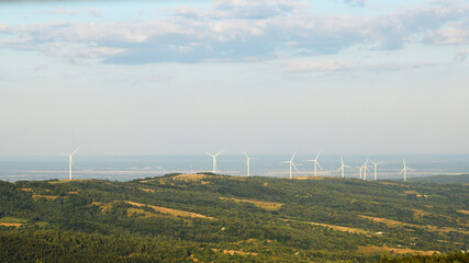 Wind turbines farm generating green renewable energy on green hills landscape under blue sky © Yanina
