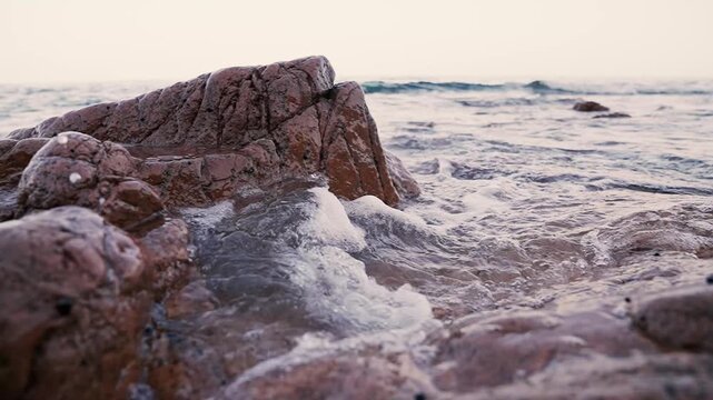 Cinematic Close Up View of Ocean Waves Splashing Over Textured Brown Rocks