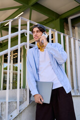 Young man in blue shirt stands outdoors, engaged in a phone conversation on campus © LIGHTFIELD STUDIOS