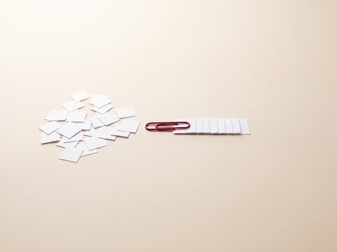Red paperclip holding a neat stack of papers on a beige surface.