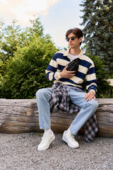 Obraz premium A young man in casual college style outfit and sunglasses sitting on log